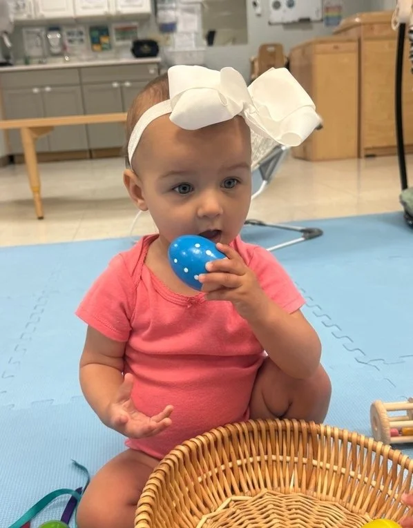 Infant exploring a colorful Easter egg during sensory play in the classroom.