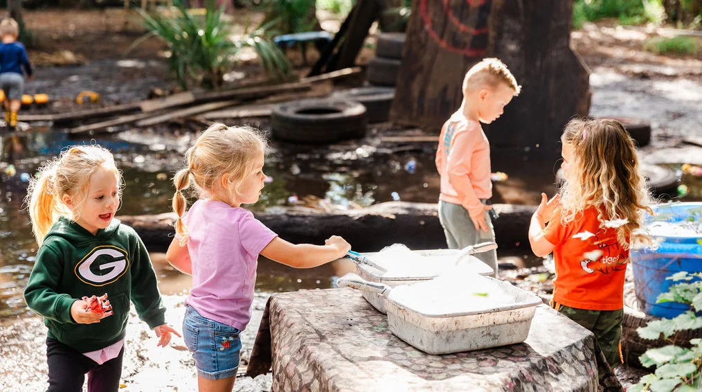 Preschool students exploring water and sand play at an outdoor nature-based learning area.