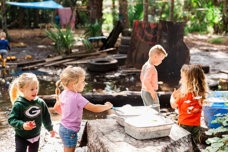Preschool students exploring water and sand play at an outdoor nature-based learning area.